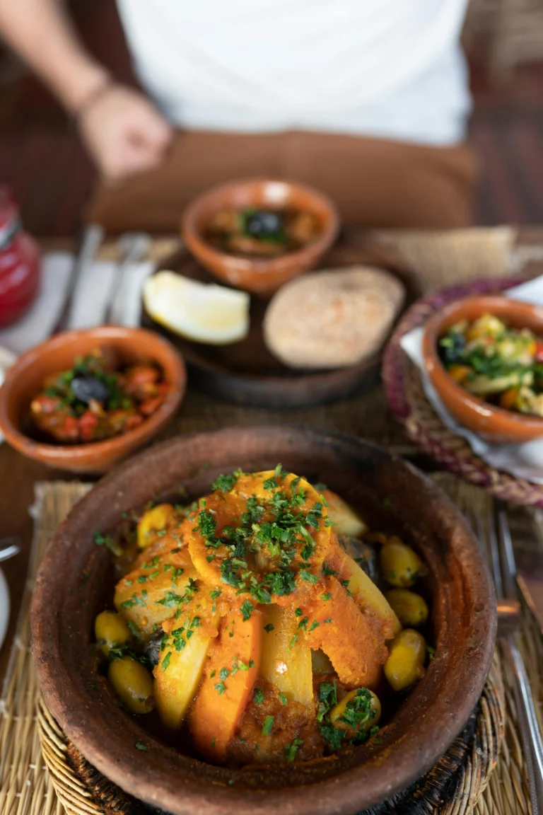 Tajine marroquí tradicional servido en un plato de barro con verduras y cuscús.