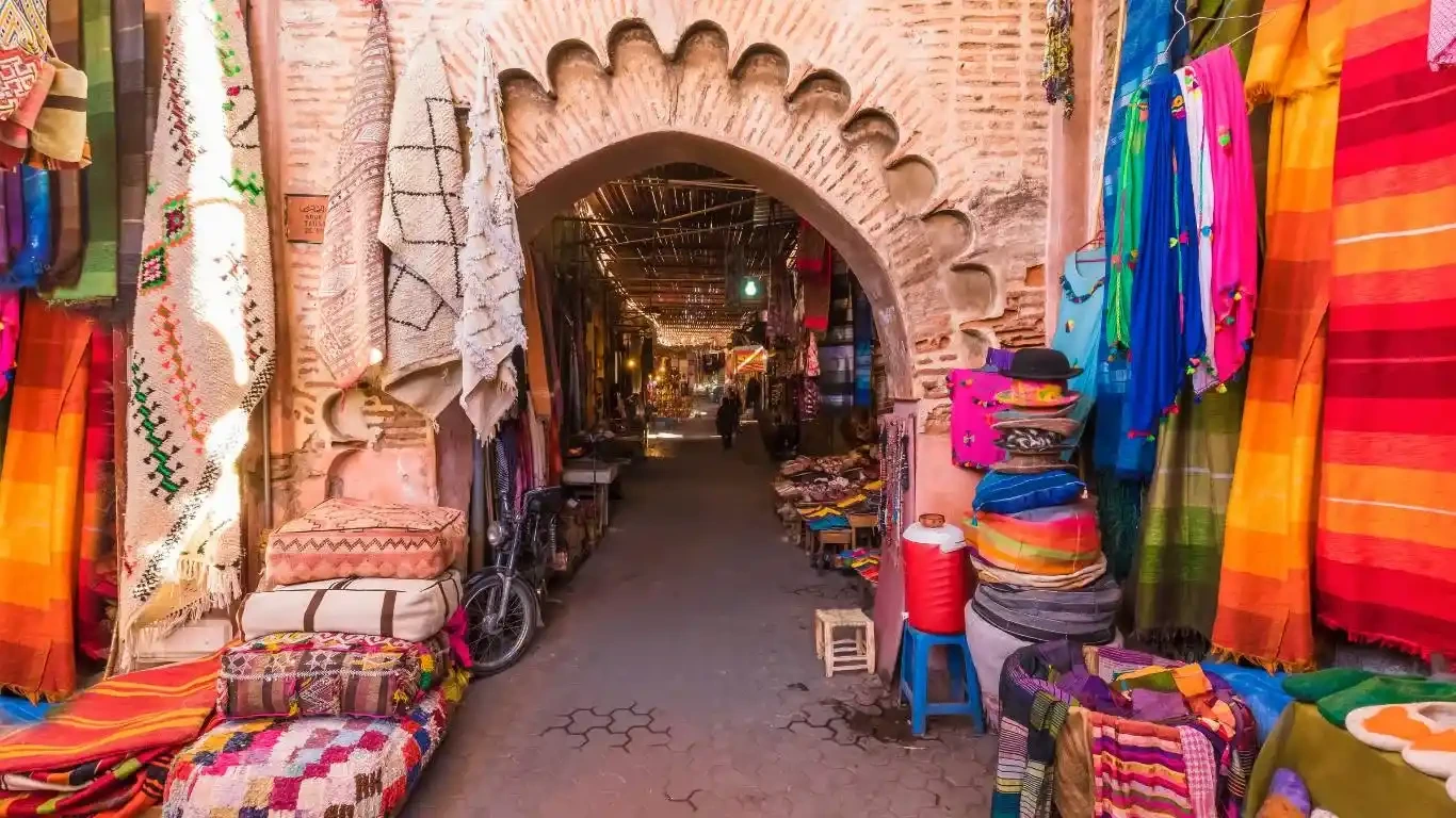Vendedor de especias en un zoco tradicional de Marrakech, con sacos de colores vivos y ambiente animado.