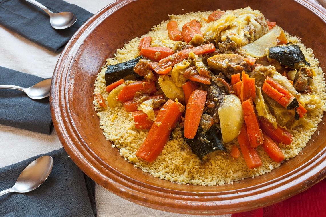 Tajine marroquí tradicional con cordero, ciruelas y almendras servido en plato de cerámica.
