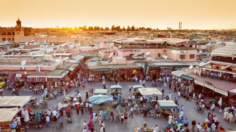 Vista panorámica de la plaza Jemaa el-Fna al atardecer en Marrakech, con puestos de comida y luces encendiéndose.